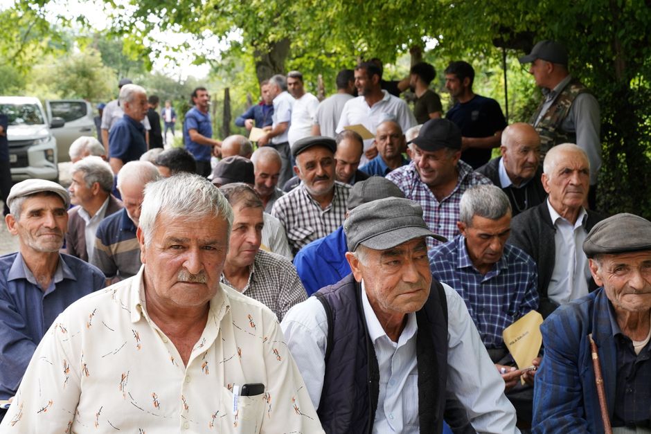 Participação Cidadã — Senior men gathered outdoors, engaging in social interaction under trees.